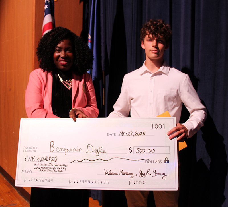 A woman on the left holds an oversize check and hands it to a young man on the right.