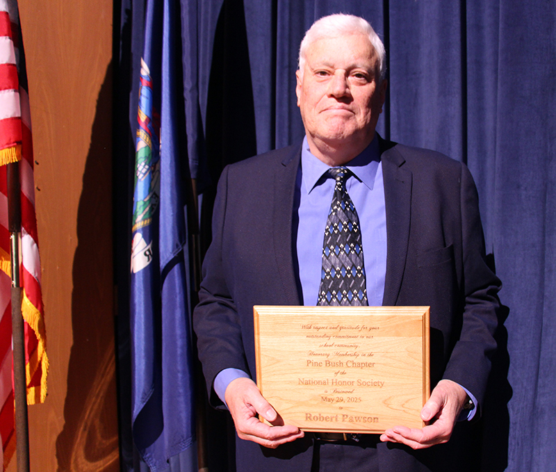A man in a blue suit and tie smiles, holding a plaque.