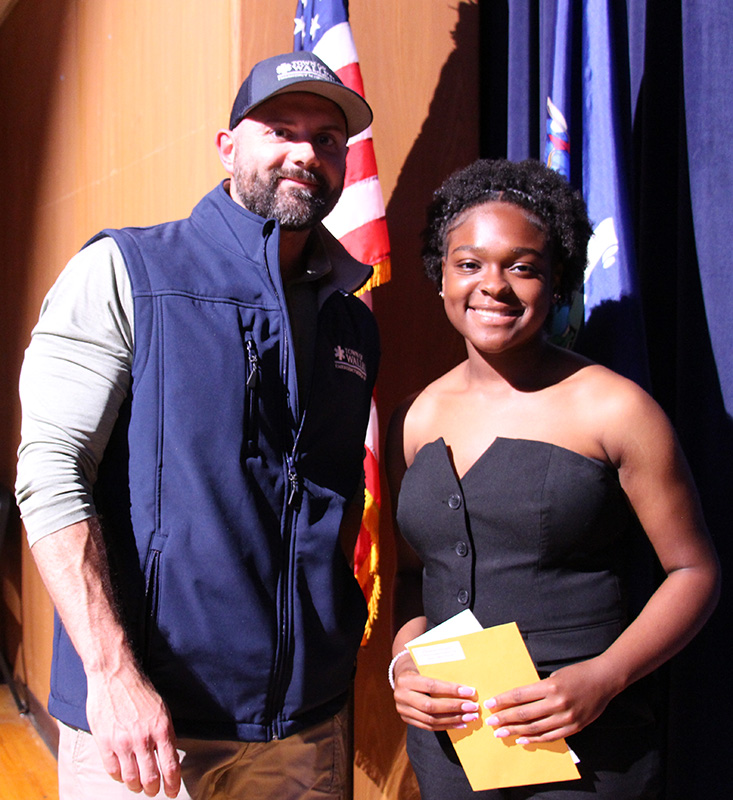 A man stands on the left with a young woman on the right. Both are smiling.