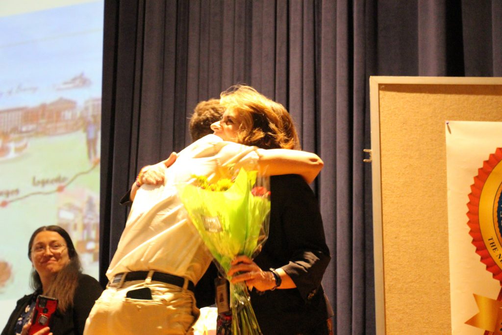 A young man hugs a woman after handing her flowers.