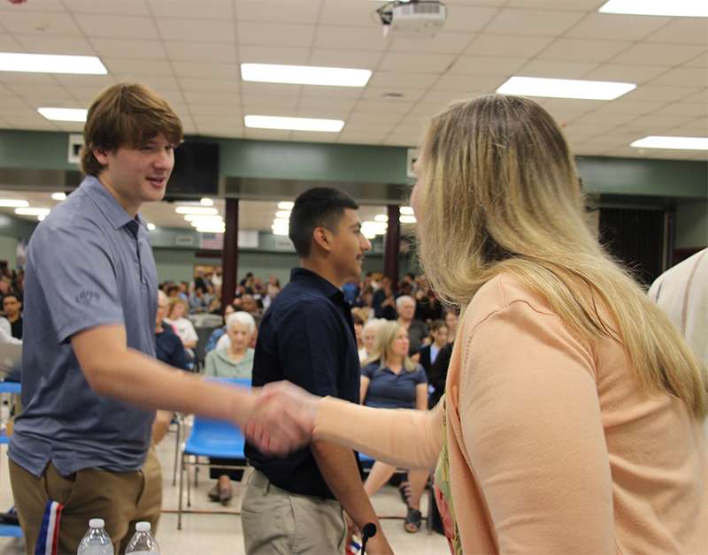A young man shakes hands with a woman with long blonde hair.