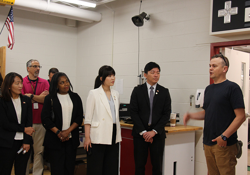A man stands to the right and talks to a group of adults in a classroom.