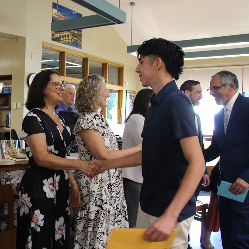 A young man wearing a blue shirt smiles as he shakes hands with a woman.