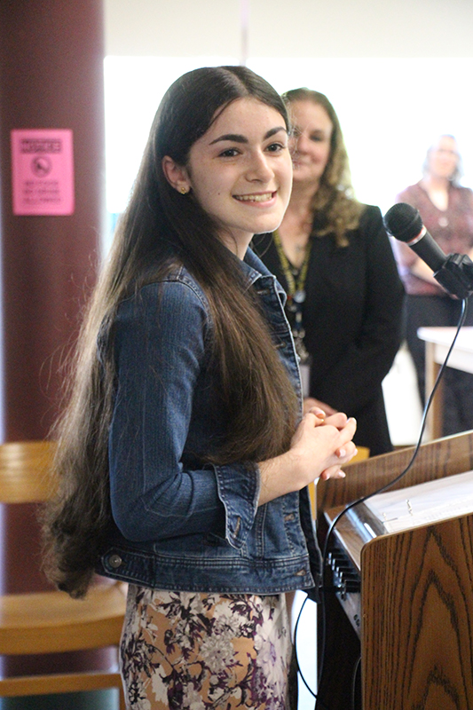 A young woman with long dark hair smiles broadly as she looks at someone off to the side.