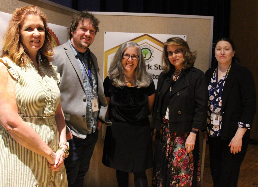 Five adults, four women and one man, stand together smiling.