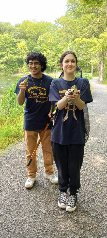 Two high school students in blue shirts hold large frogs they found in the lake.
