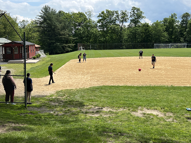 High school students and some teachers play kickball on a large baseball field.