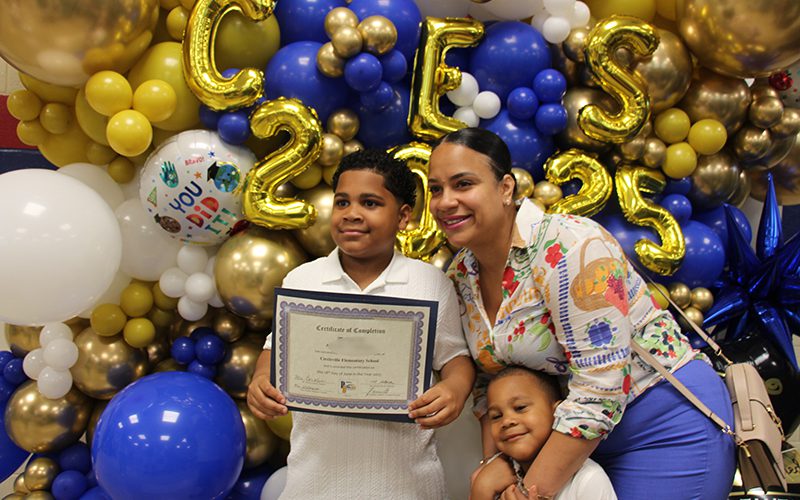 A woman and two kids stand in front of a big blue and gold balloon display that says CES 2025.