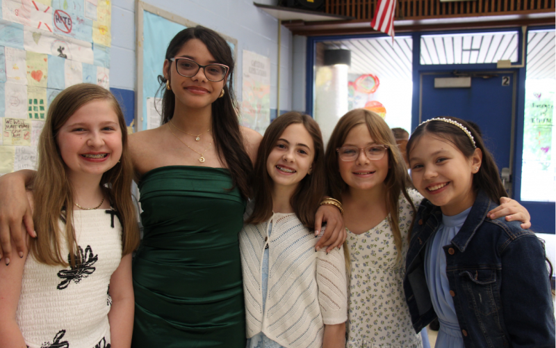 A group of fifth-grade girls stand together smiling.