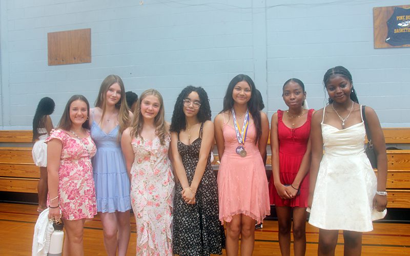 A group of seven eighth-grade girls all dressed up stand together smiling.