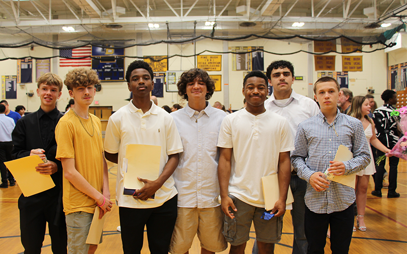 A group of seven eighth-grade boys stand together smiling.