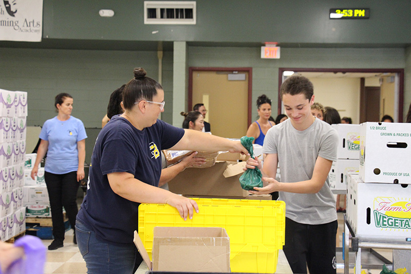 A woman hands a bag of groceries to a young man.