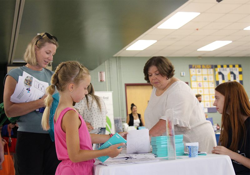 A woman behind atable talks to a woman and a little girl.