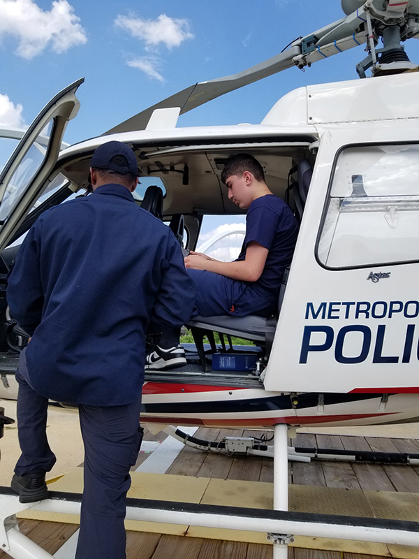 A high school students sits in a Metro DC Police helicopter while an officer explains the controls to him.