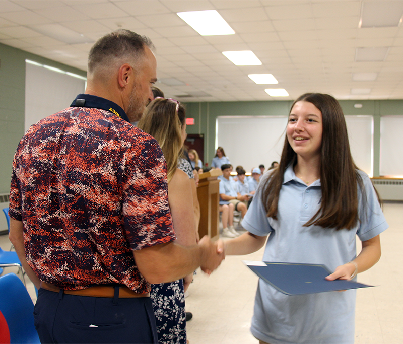 A high school girl shakes hands with a man. They are both smiling.