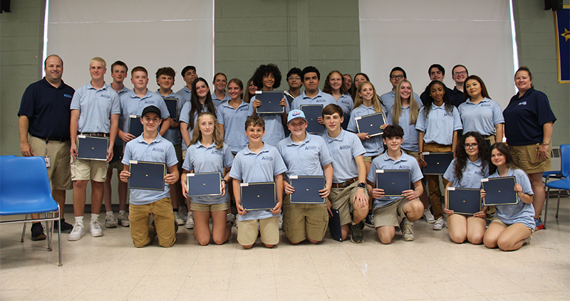 A group of 30 high school students, a group kneeling on the floor and the others standing behind them, along with four instructors , stand together . Several are holding certificates.