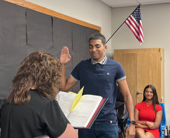 A young man raises his right hand and takes a oath, given to him by a woman whose back is to the camera.
