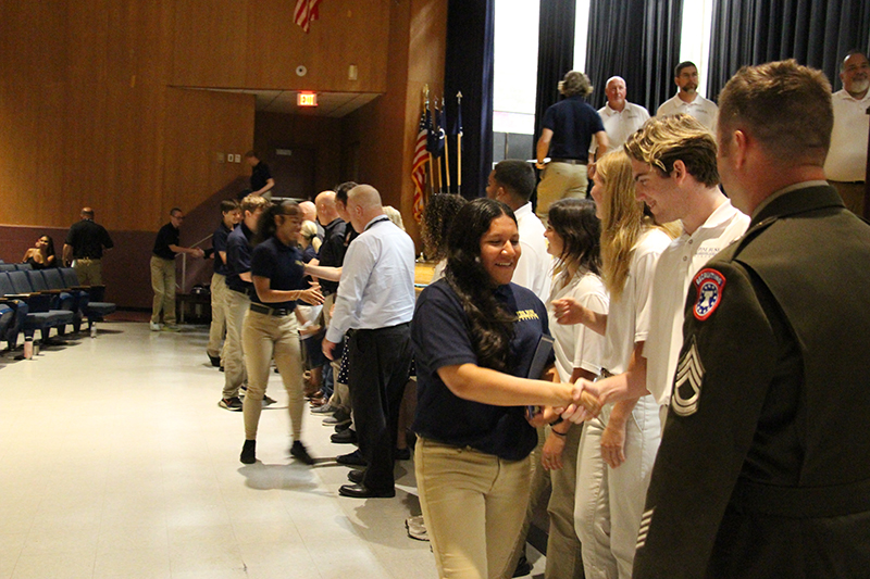 A high school student shakes hands with adults and receives a certificate.