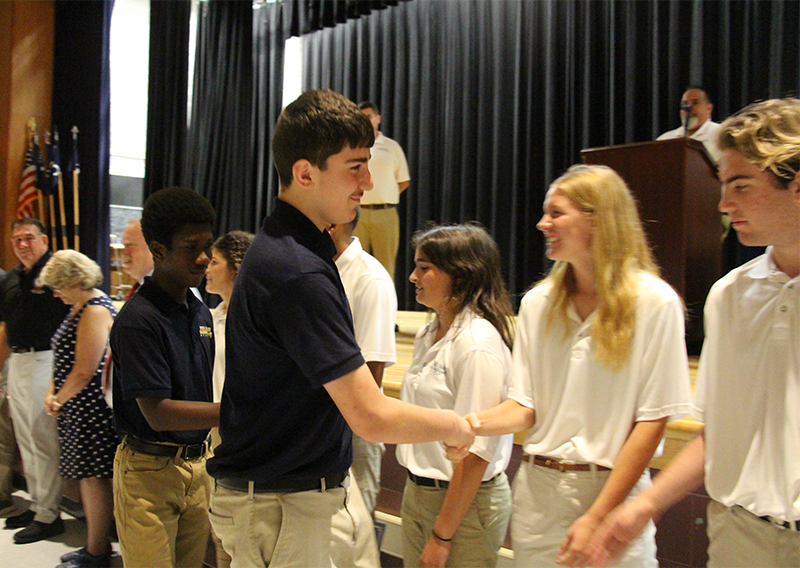 A high school student shakes hands with adults and receives a certificate.