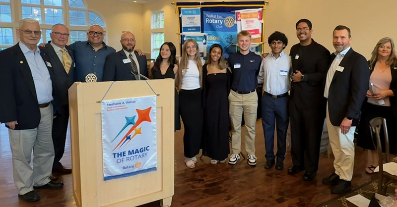 A group of six high school seniors stand with six adults. They are all smiling.