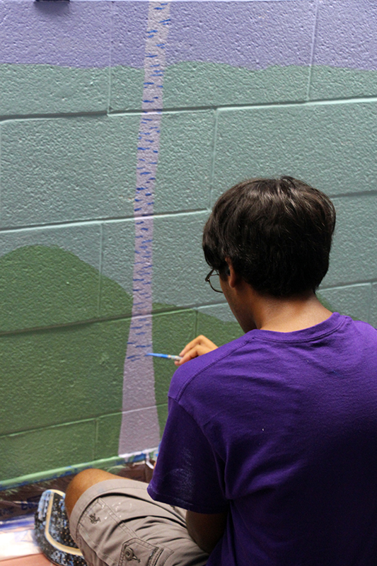 A young man paints a birch tree on a wall.