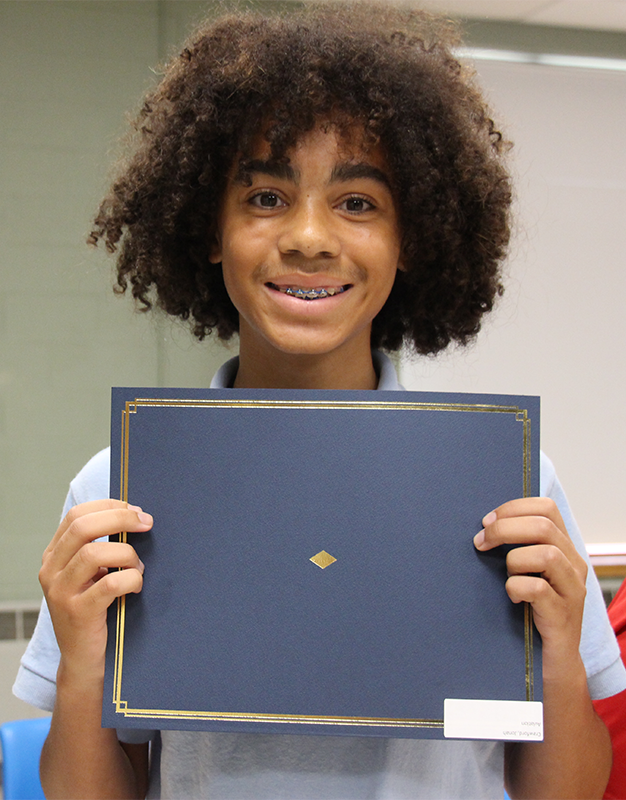 A high school student smiles holding a certificate.