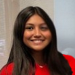 A young woman with long dark hair smiles. She is wearing a red shirt.