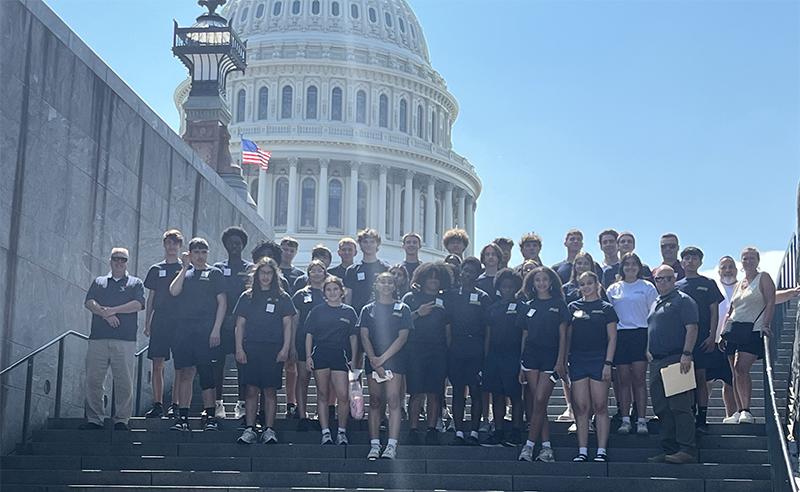 A large group of high school students stand on the steps to the US Capital.