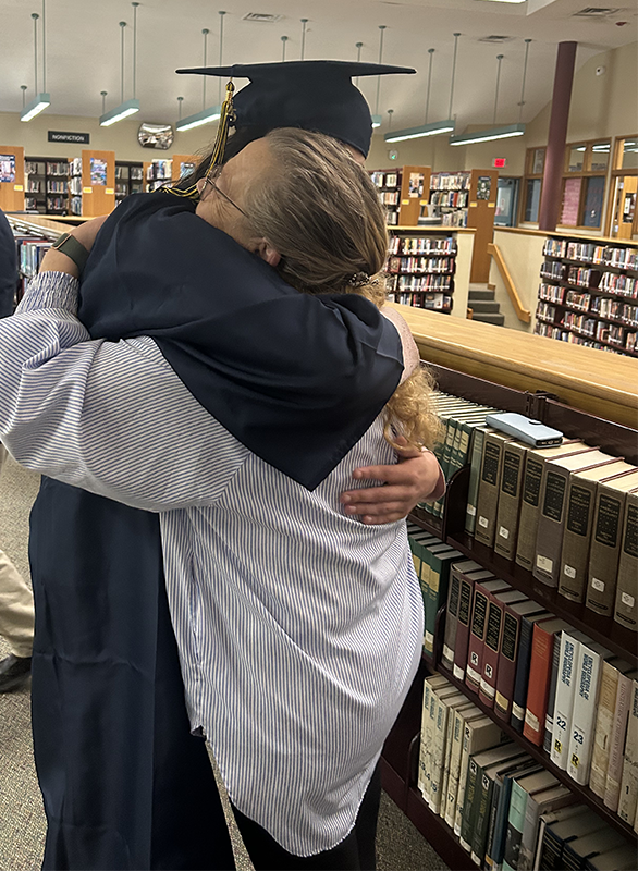 A young man in a blue cap and gown hugs a woman.