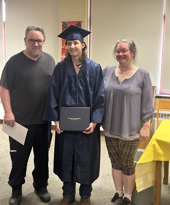 A young man in a blue cap and gown smiles and holds his diploma. On either side is a man and woman. They are also smiling.