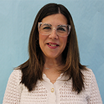 A woman with longer dark hair smiles. She is wearing a white shirt and glasses.