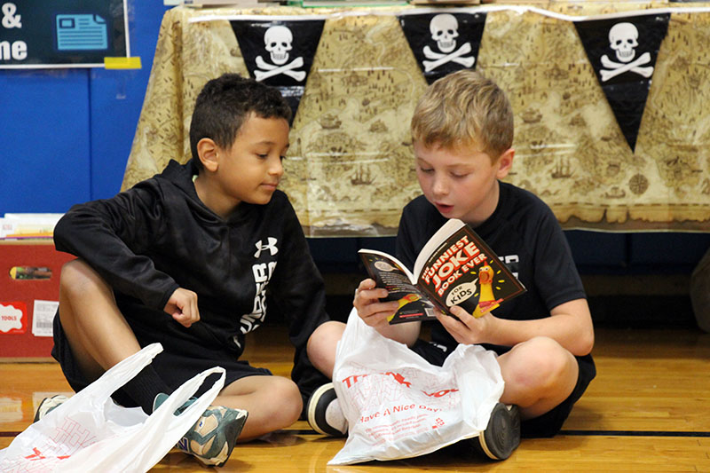 Two boys sit on the floor looking at a book.