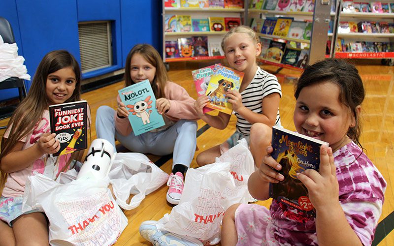 Four elementary age girls show the books they bought. They are smiling.