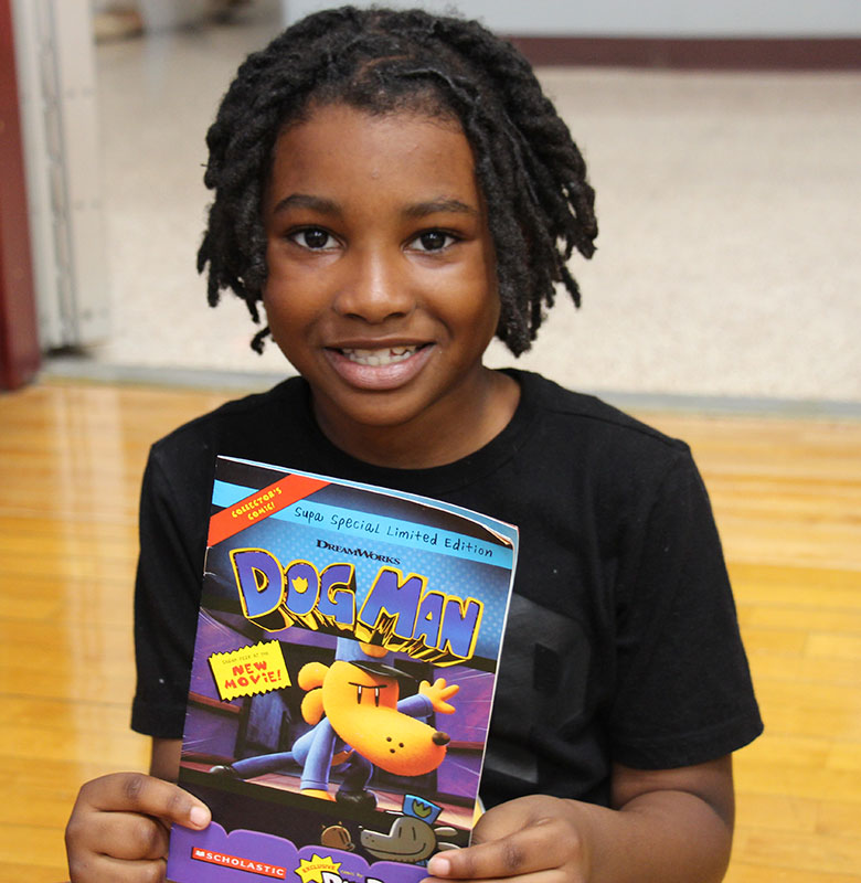 An elementary students smiles and holds up a book.