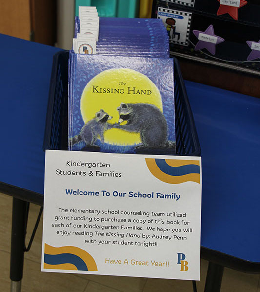 A rack with books on it. The book is The Kissing Hand and has a picture of a large and small raccoon.