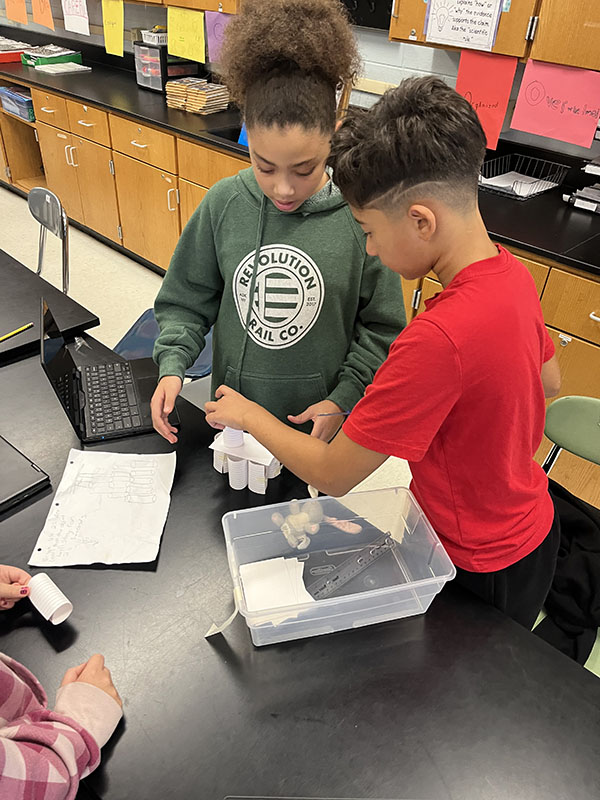 Two sixth-grade boys work together building a tower of index cards.