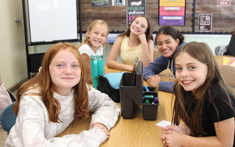 Five middle school girls sit at a table and smile.