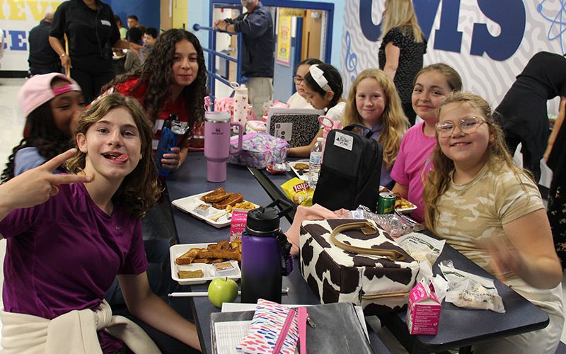 Crispell lunch girls at the table A large table of middle school girls eating lunch. There are trays of food - french toast sticks - on the table.
