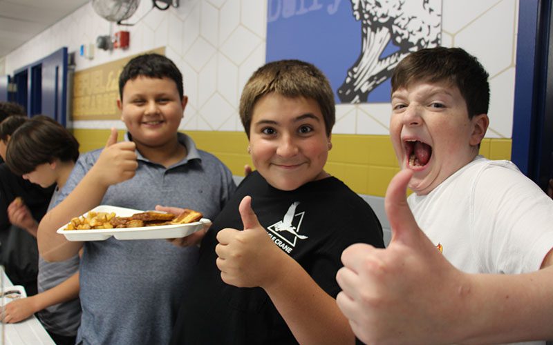 Crispell lunch silly boys Three middle school boys smile and make funny faces giving thumbs up while getting their lunch.