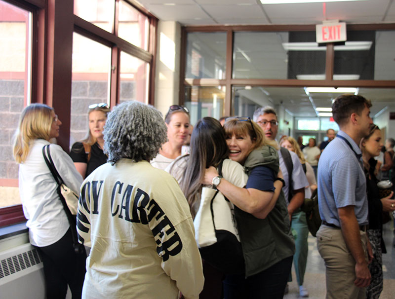 A group of people meet up in a hallway. Some are hugging each other.