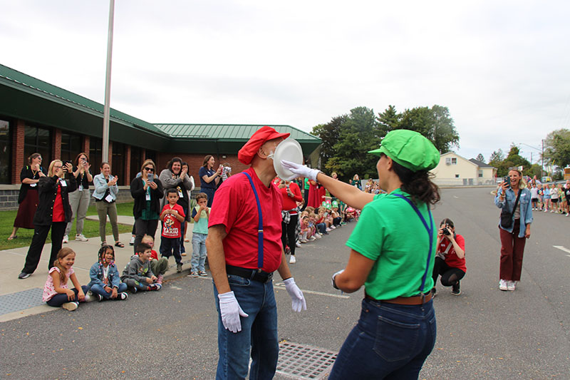 A woman dressed as cartoon character Luigi smooshes a pie into a man dressed as Maria in red.