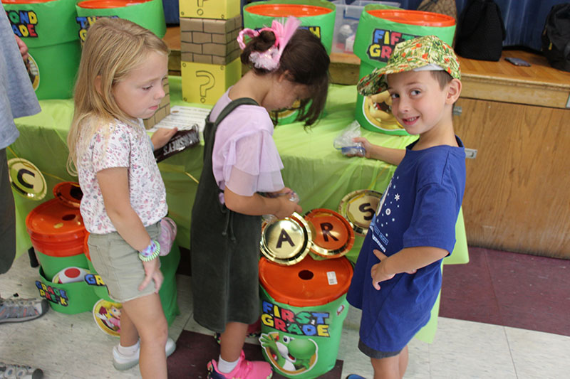 Younger elementary students look at decorated containers to put their coins in.