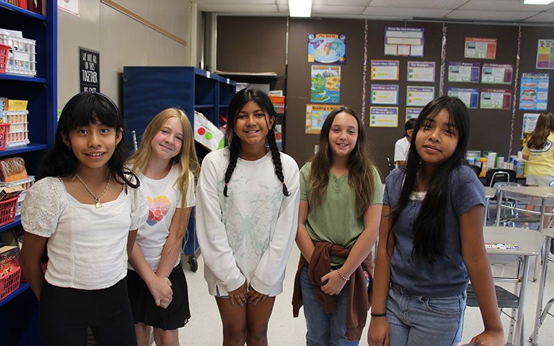 Five fifth-grade girls stand together smiling.