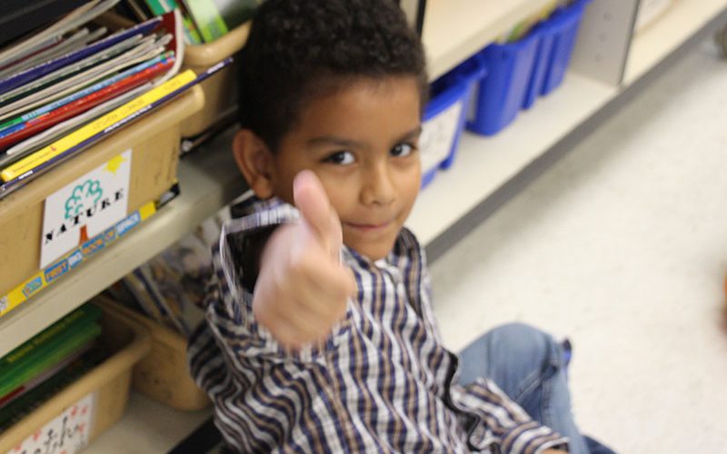 A young elementary age boy gives a smile and a thumbs up.
