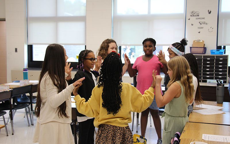 A group of fourth-grade girls in a circle doing a team building exercise, meeting hands with each other.