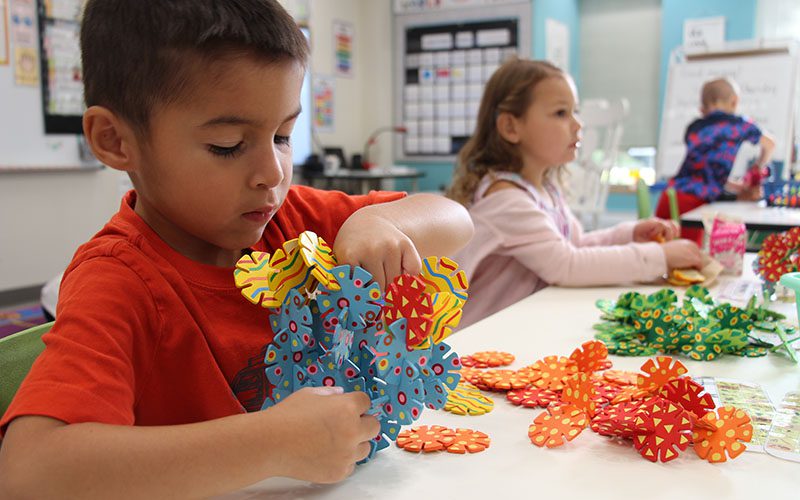 A kindergarten boy holds something he made out of little colorful discs.
