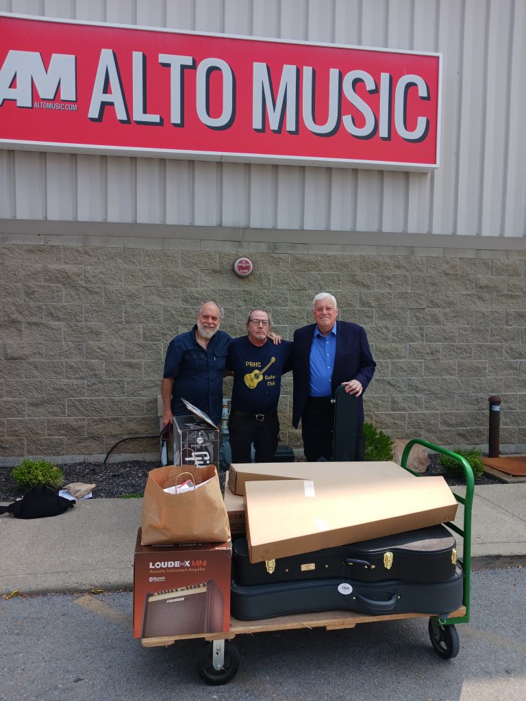 Three men outside of a building with a lot of boxes in front of them. The sign on the building says Alto Music.