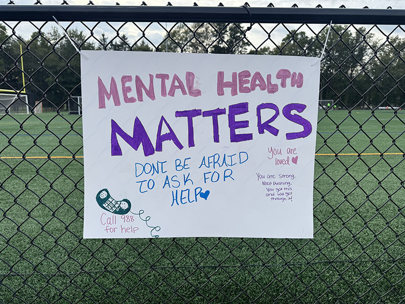 A poster on a chain-link fence. It says Mental Health Matters. Don't be afraid to ask for help. Call 988 for help. You are loved. You are strong. Keep pushing. You got this and will get through it!