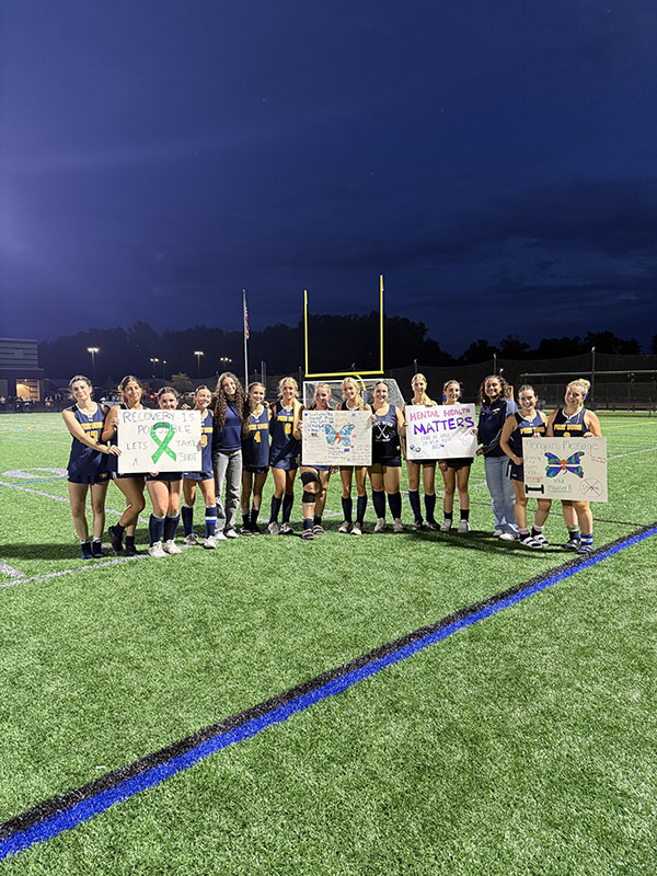 A team of field hockey players hold up four different posters about mental health.