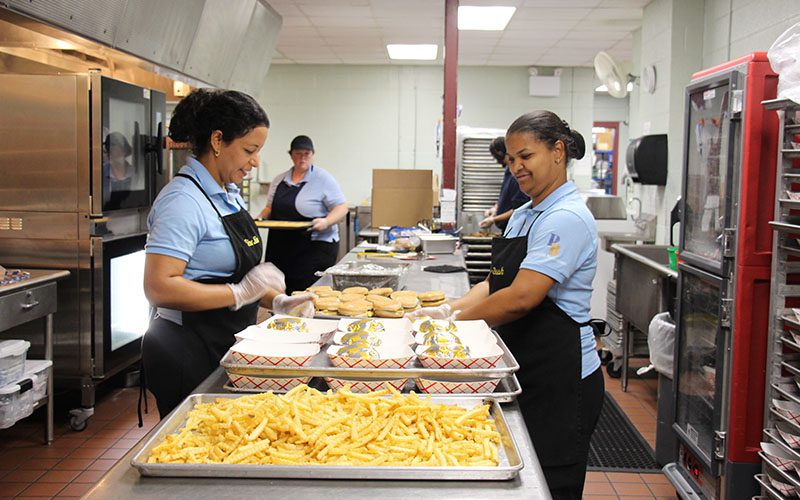 PBHS food services prepping the burgers and fries Two women in a busy kitchen. They are making hamburgers and fries.